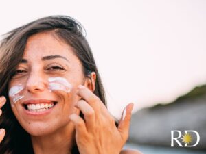 Smiling woman applying sunscreen to her face to prevent melasma from appearing.